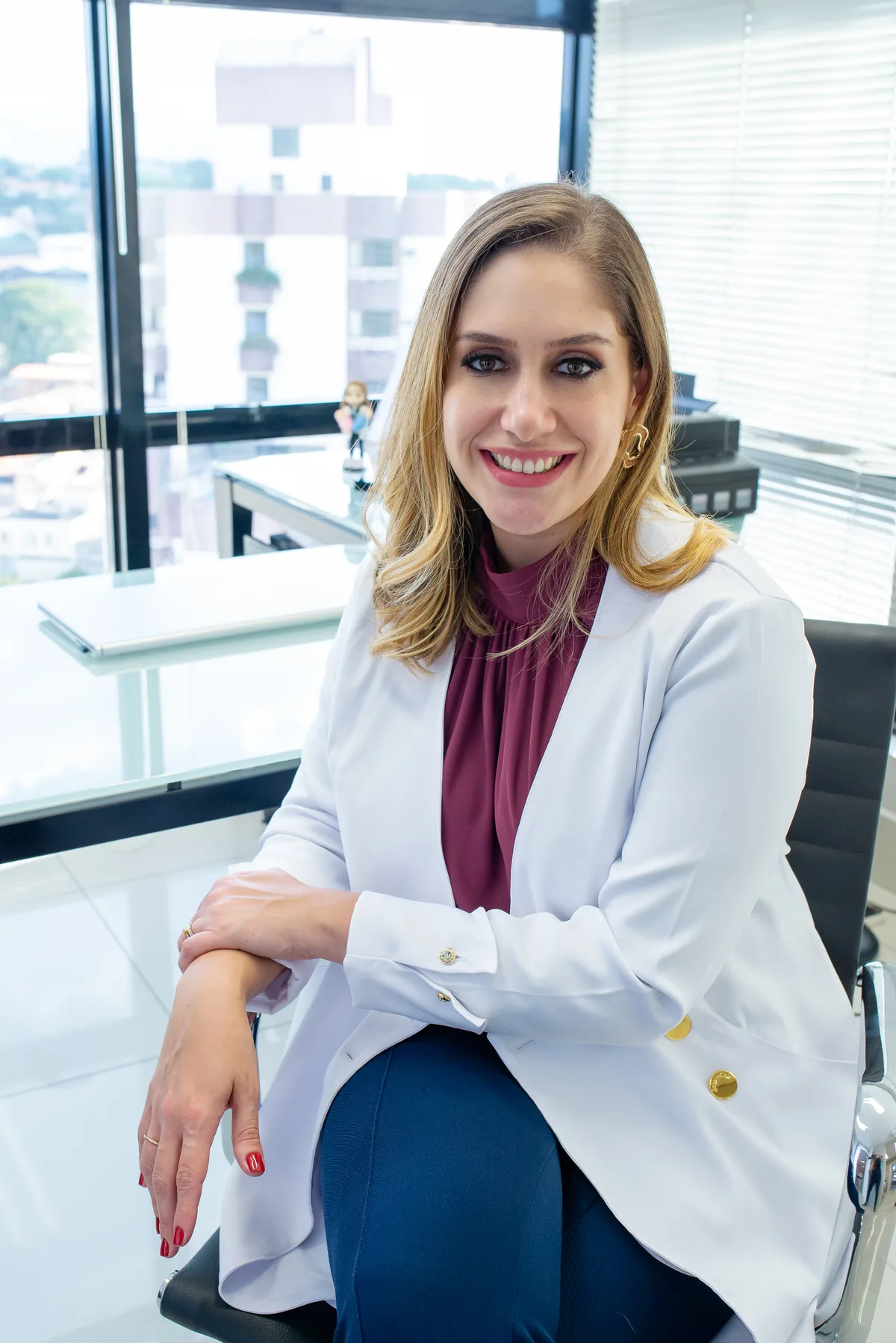 Dra. Lívia Levada Ferreira, ginecologista e obstetra em Jundiaí SP, de jaleco branco sorrindo no consultório